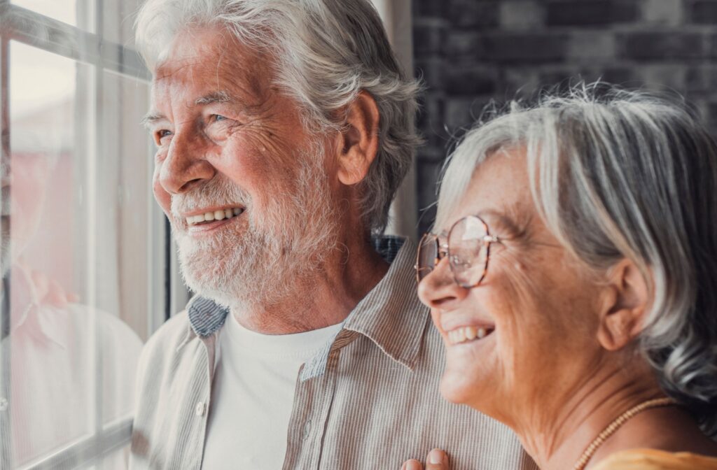 An older couple looking out the window and smiling after moving into their new home in assisted living.