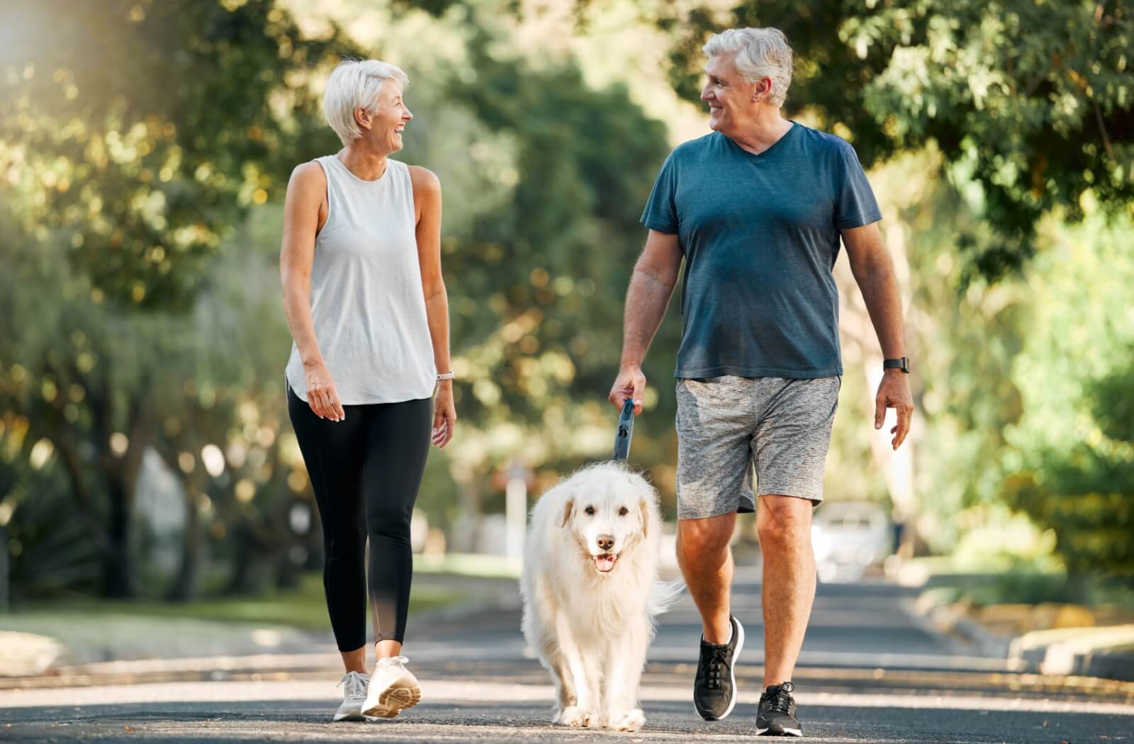 2 older adults smiling while out for a walk with their fluffy white dog