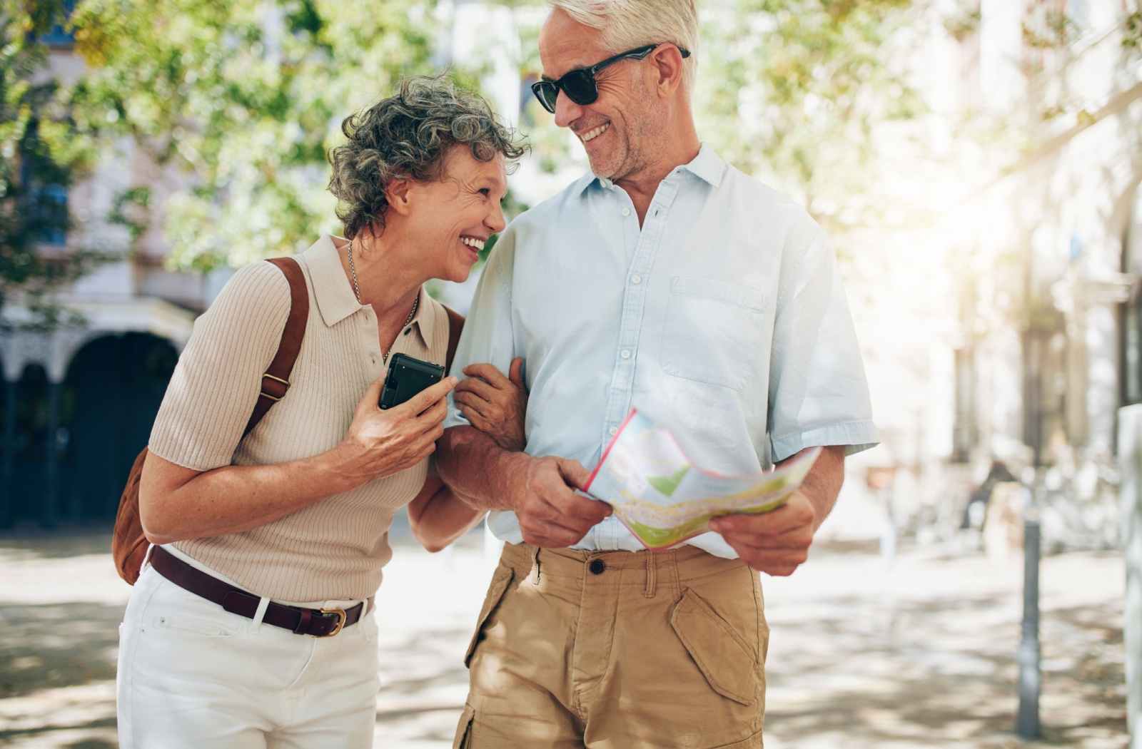 A giggling senior couple smile at each other while consulting a paper map with a pre-planned route for exploring their city