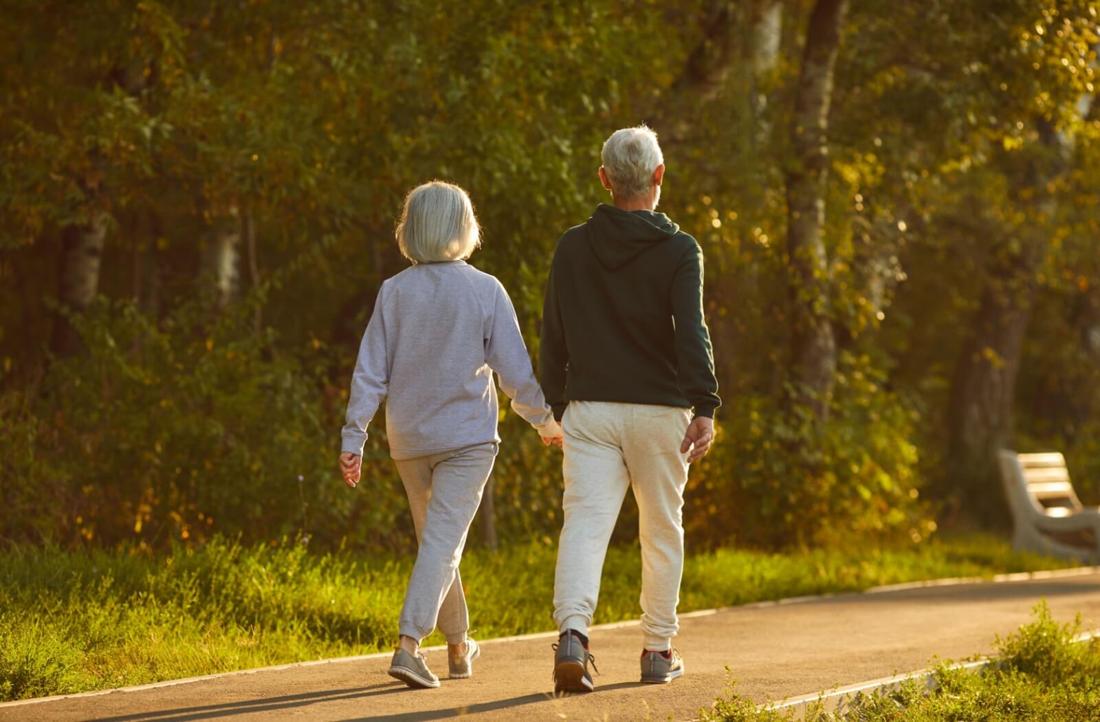 A senior couple holds hands while walking through a state park, enjoying the sunset and each other’s company