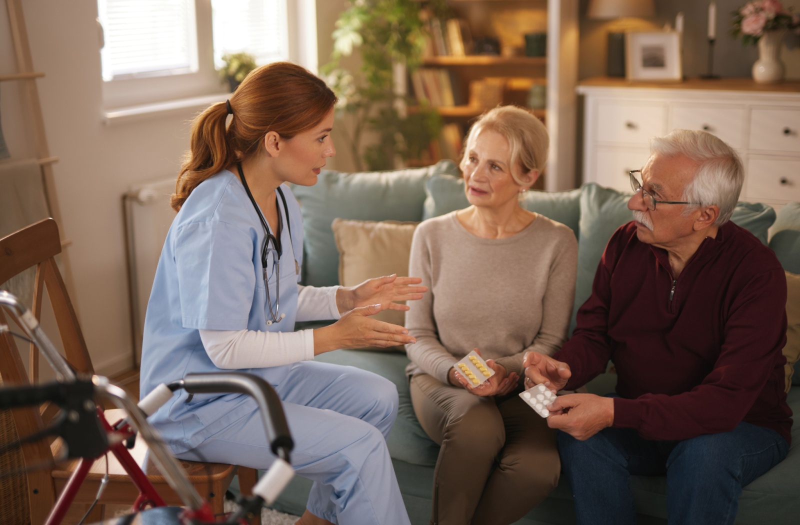 A caregiver sits beside an older couple in their living room and discusses what they can expect from short-term respite care