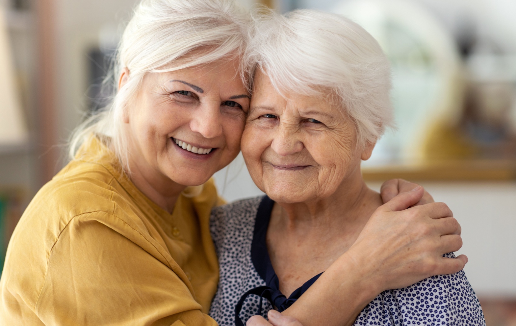 An adult child embraces their senior parent as they both smile toward the camera.