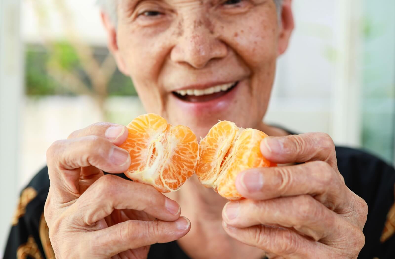 A smiling senior enjoys a juicy orange and gets their daily dose of vitamin C.