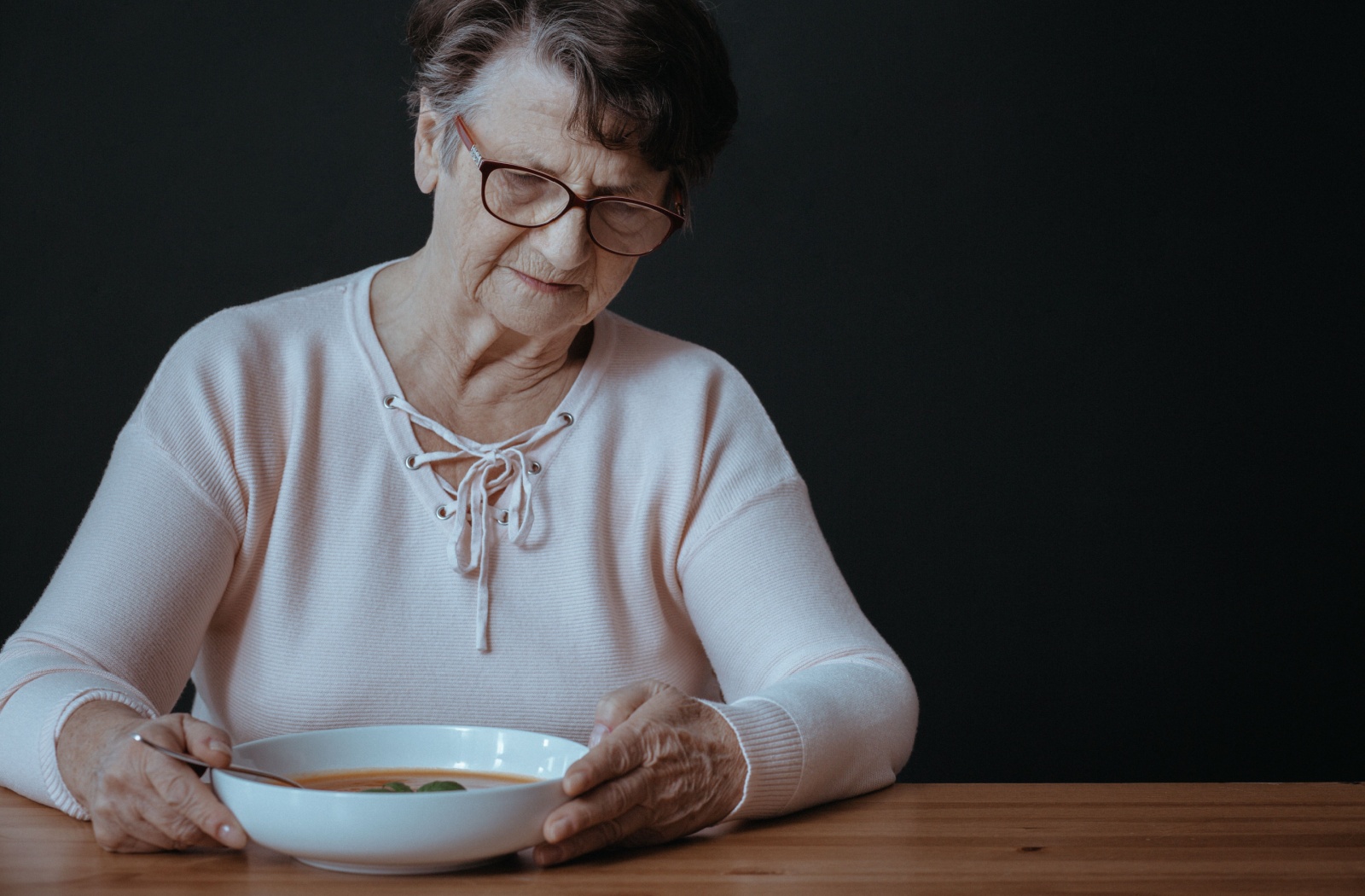 An older adult with dementia looking at a bowl of soup with decreased appetite.