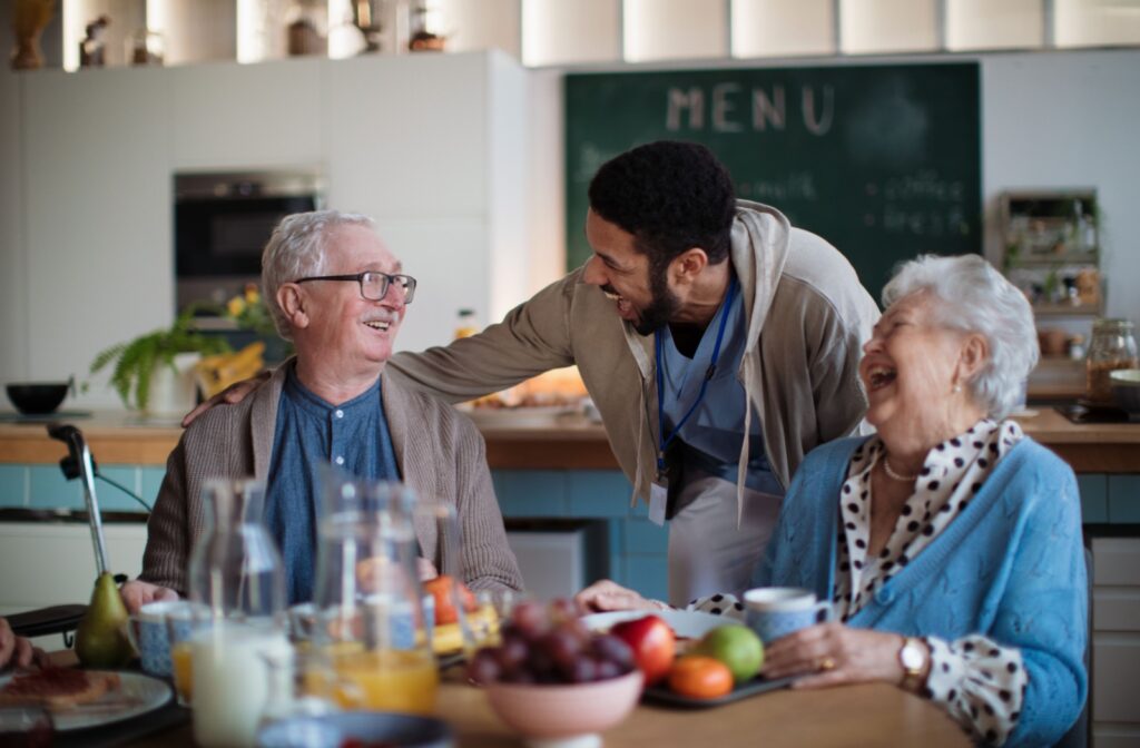 A staff member in senior living laughing with an older couple during breakfast.