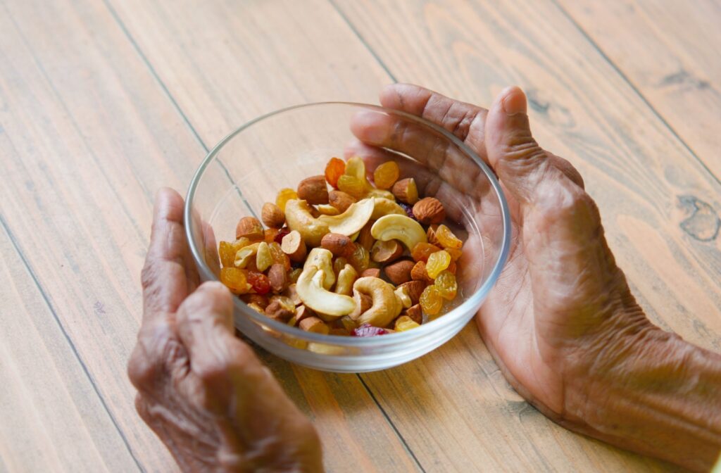 A close-up view of an older adult's hands cupping a bowl of mixed nuts on a table.