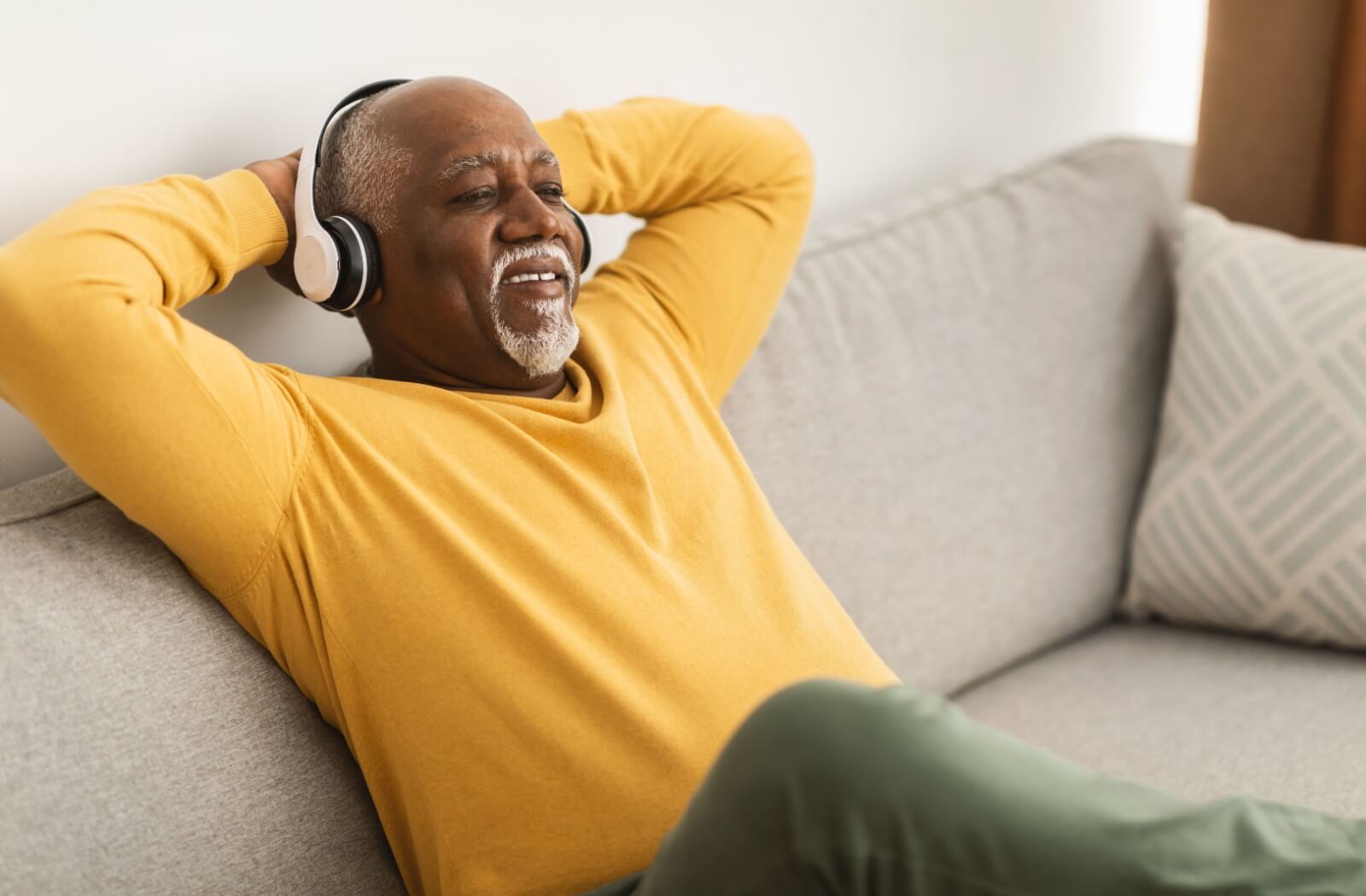 A smiling senior relaxes on their couch and listens to an engaging audiobook with headphones.