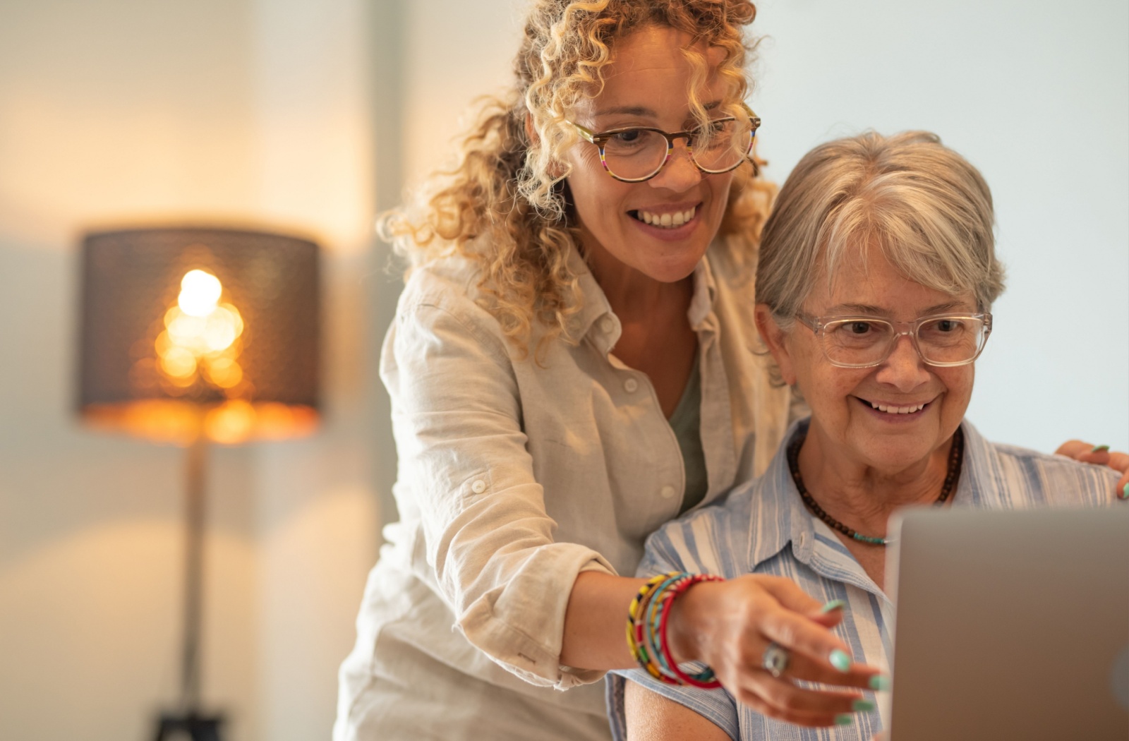 A smiling adult child helping their older parent research assisted living on a laptop.