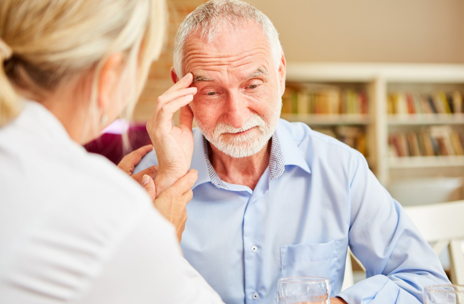 An older adult gently touches their forehead in confusion during a healthcare checkup to diagnose the cause of their hallucinations